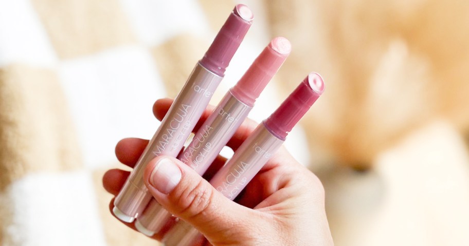 hand holding up three sticks of Tarte Maracuja Juicy Lip Balms