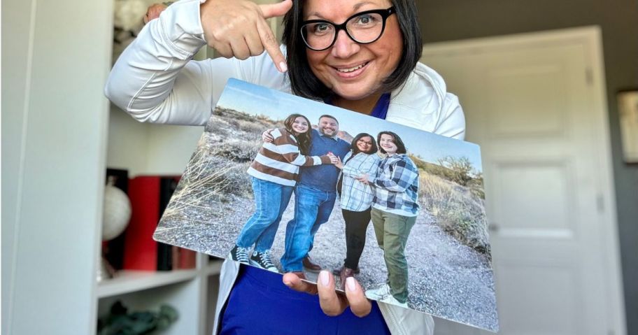 Woman hold a Walgreens metal photo print featuring a family with one hand while pointing at it with the other