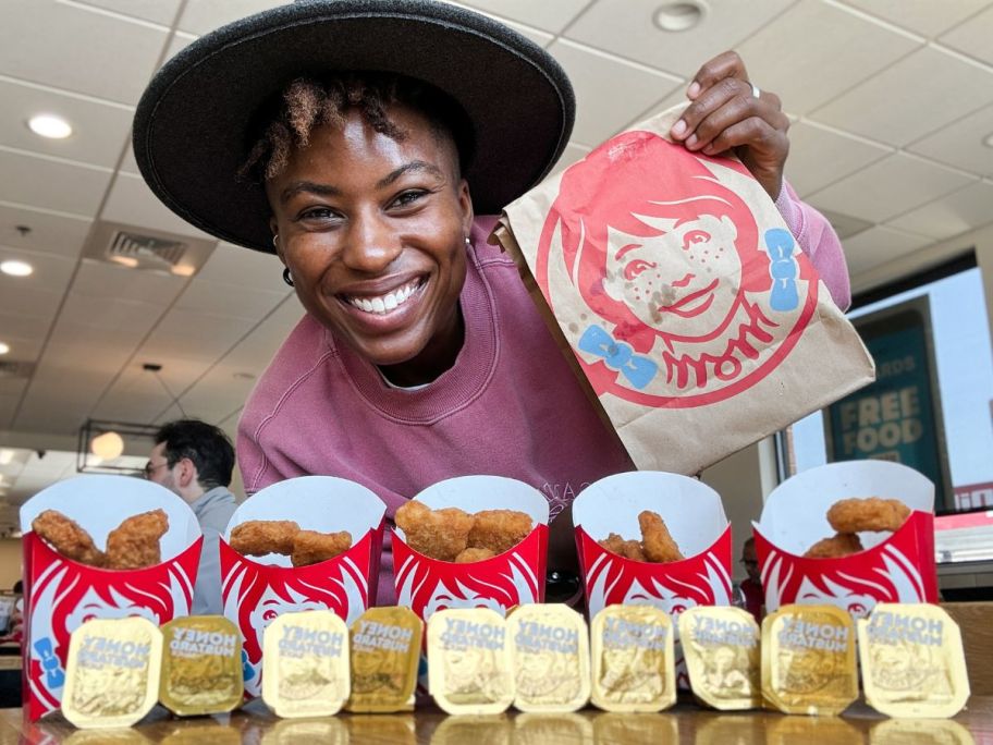 Woman holding a wendy's bag with 5 cartons of chicken nuggets and many sauce cartons lined up in front of her