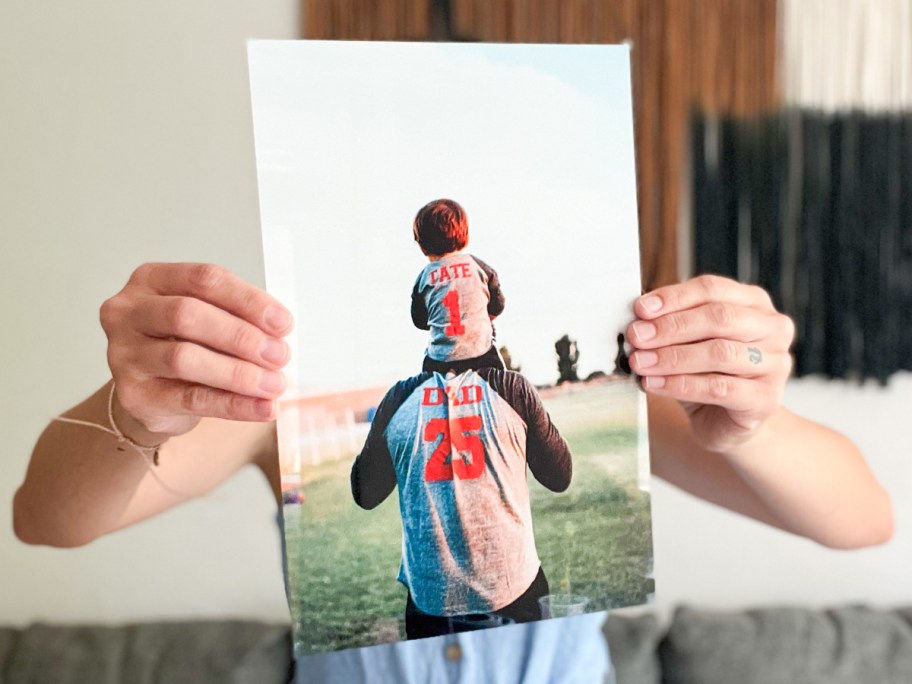 two hands holding metal print in front of face