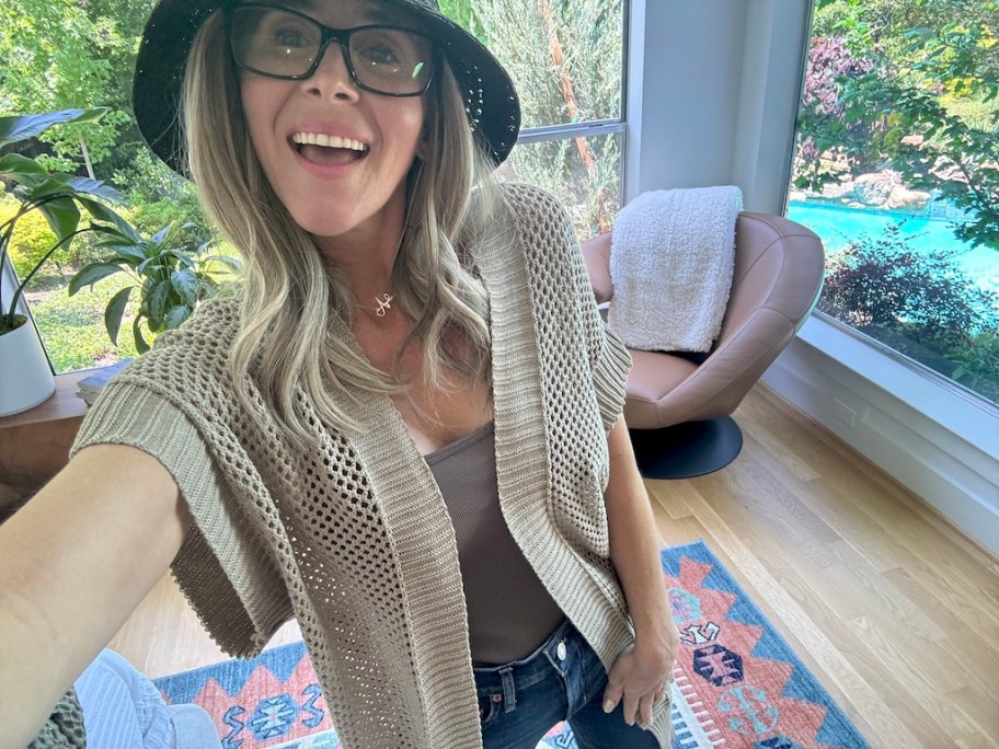 woman in a crochet duster posing for a selfie in front of an accent chair