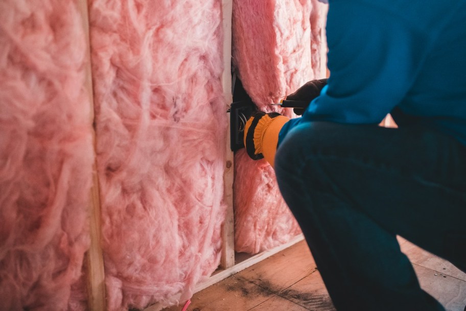 close up of man putting pink insulation into studded wall