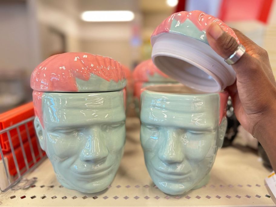 a womans hand holding up the lid to a Frankenstein head-shaped ceramic food vessel