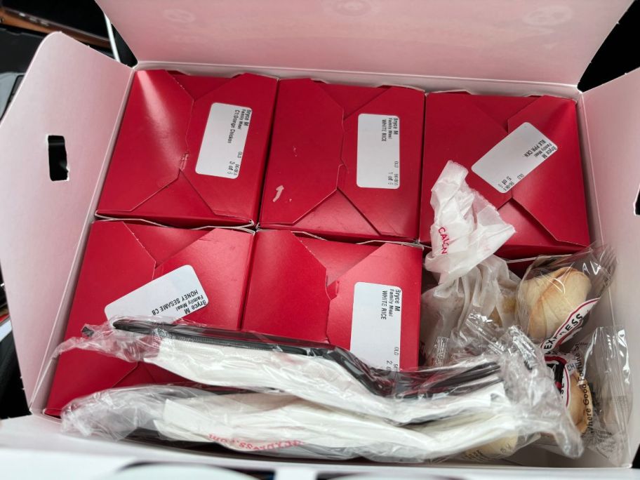 Panda Express family meal box open on a kitchen counter showing individual containers of food, and fortune cookies, along with disposable untensils.