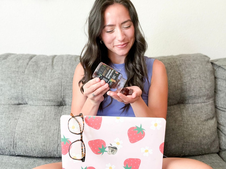 woman pouring gummies in hand from bottle with laptop in front of her