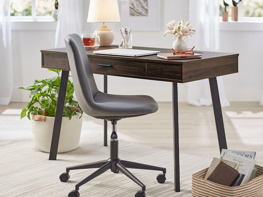 brown writing desk with gray chair in front of it and lamp on top