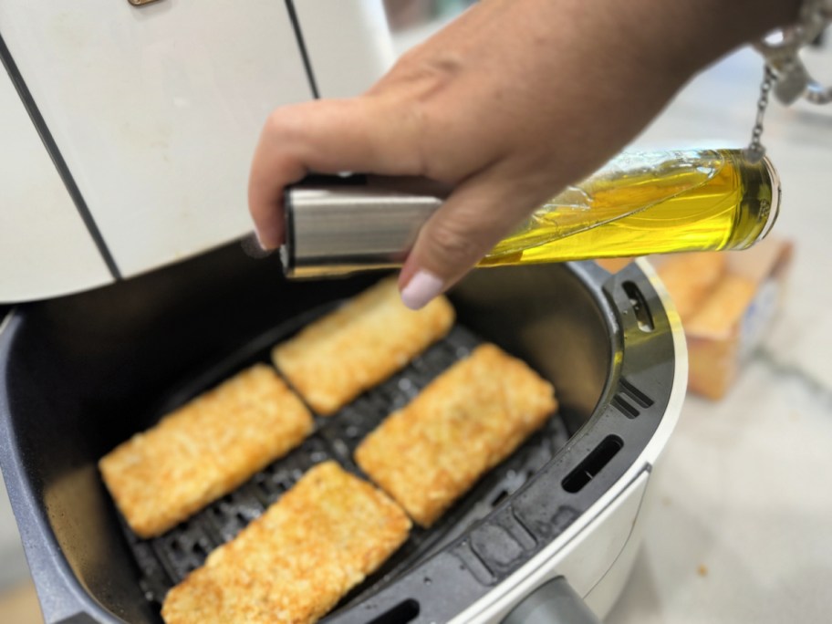 spraying frozen hash browns with oil spray inside air fryer