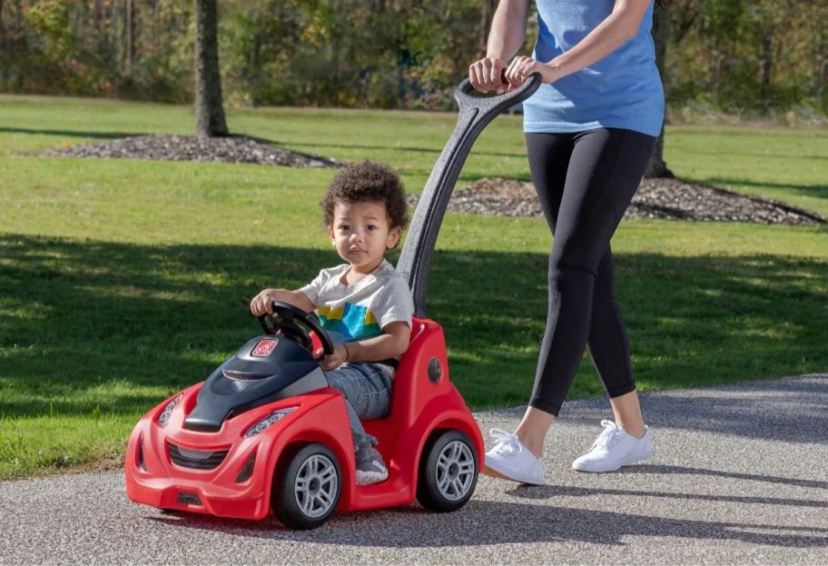 a woman pushing a toddler in a red step2 