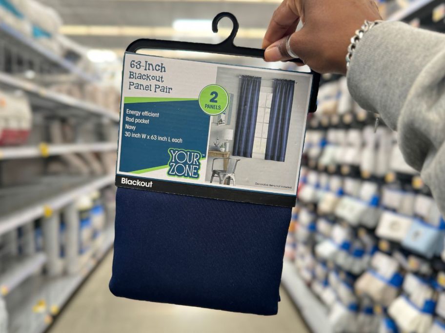 walmart Your Zone Solid Blackout Rod Pocket Curtain Panel Pair in blue being held by hand in store aisle