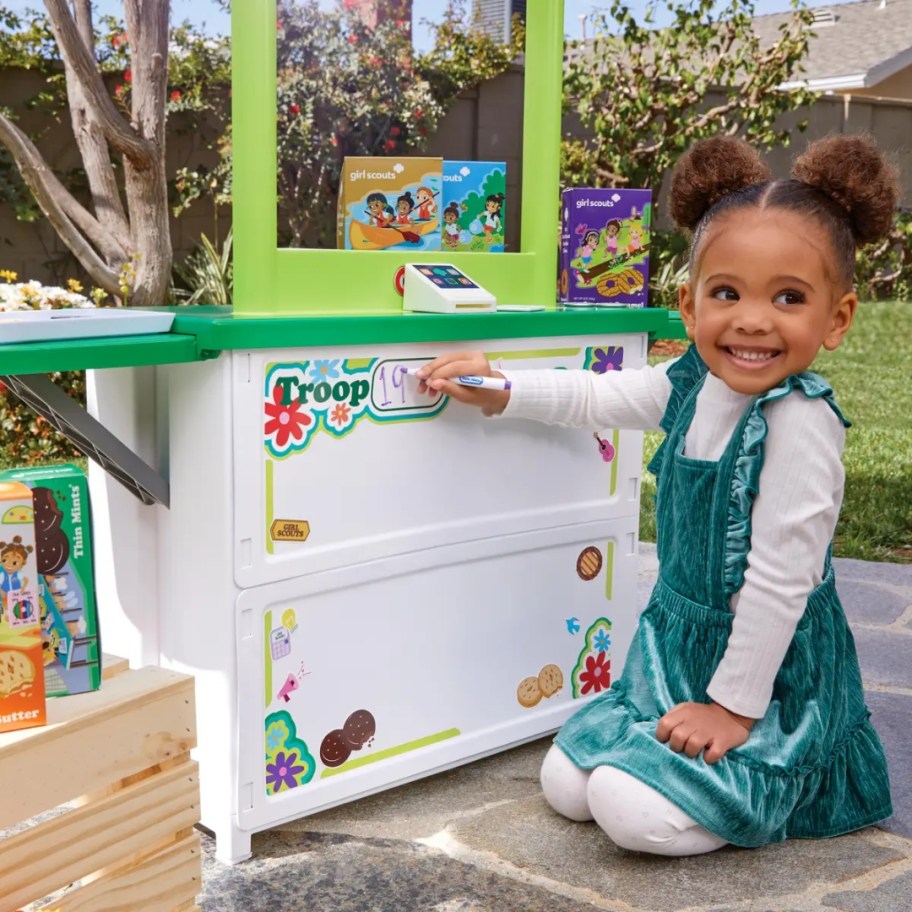 little girl writing on the front of a Girl Scout Cookie booth