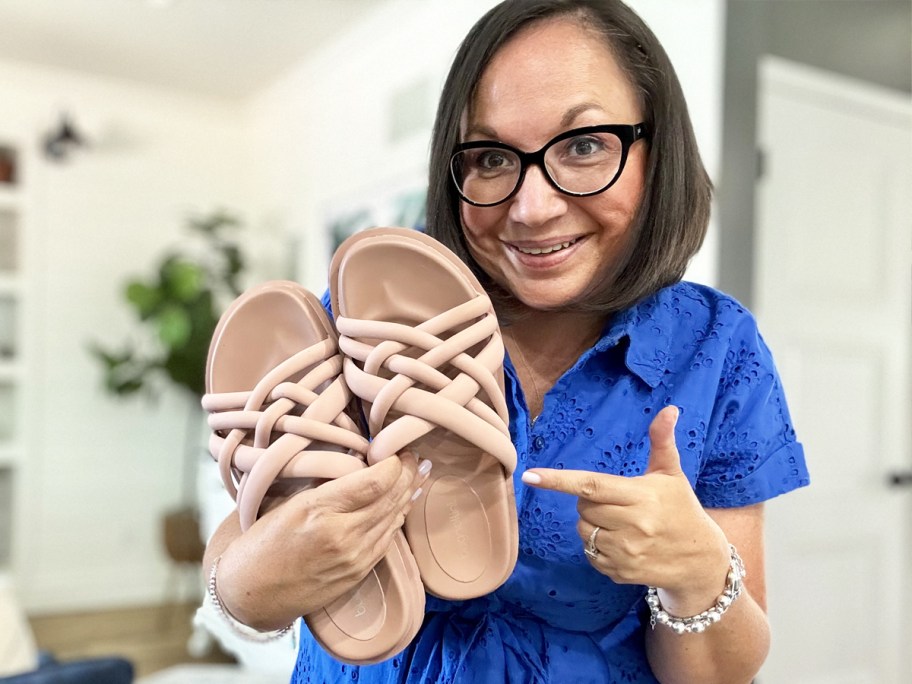 woman holding up and pointing to a pair of woven slides