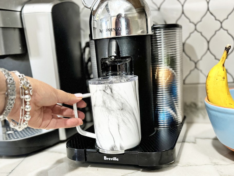 woman grabbing marble print mug from under nespresso machine