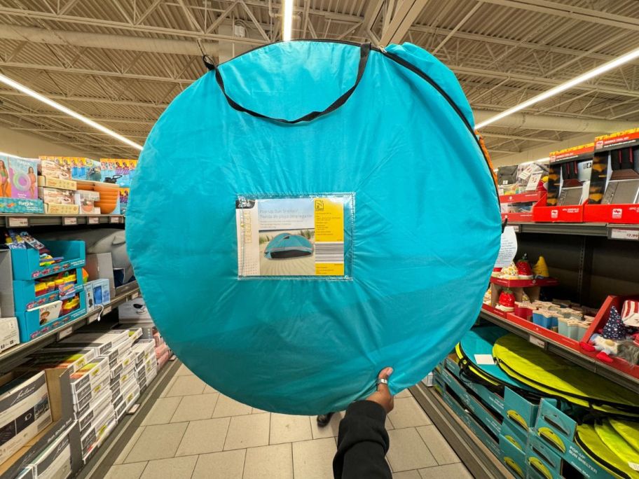 A person holding up a Crane Beach Pop Up Shelter in blue