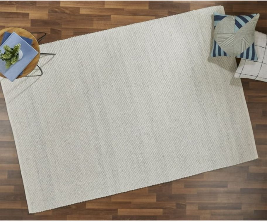 a natural colored area rug with pillows on a hardwood floor