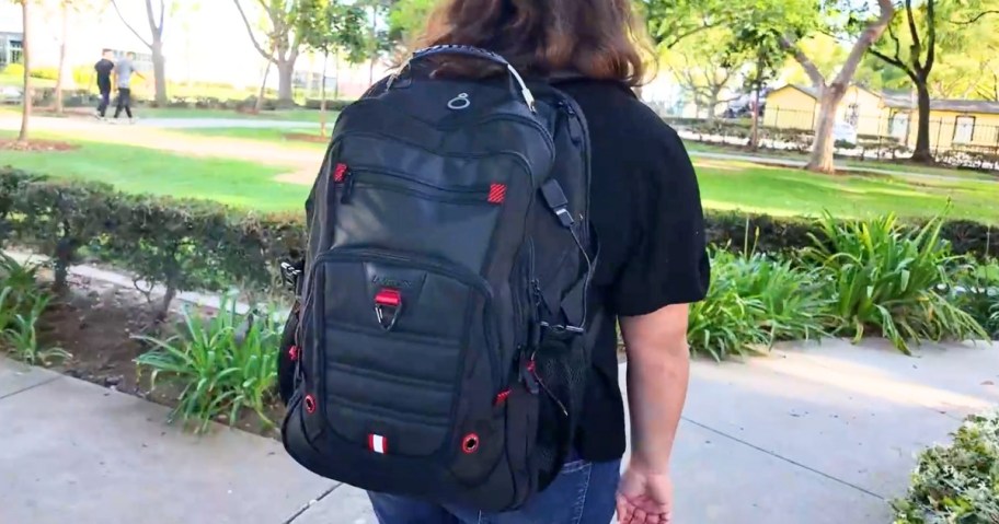 person walking outdoors wearing a large black backpack with red accents