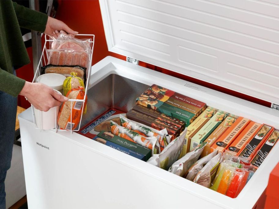 woman standing next to Hotpoint 4.9-cu ft Manual Defrost Chest Freezer in White holding a frozen food item above open freezer