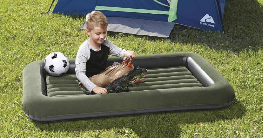 Little boy sitting on green air mattress and playing with toys while outside in yard