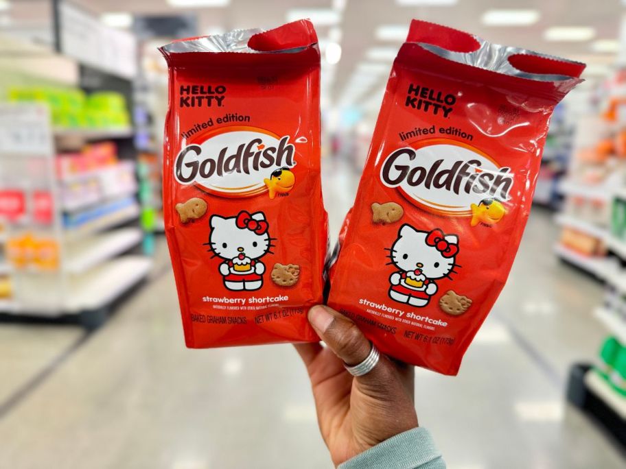 A hand holding up 2 bags of Limited Edition Goldfish Hello Kitty Strawberry Shortcake Grahams