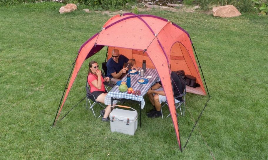 4 people sitting at a picnic table underneath a beach tent