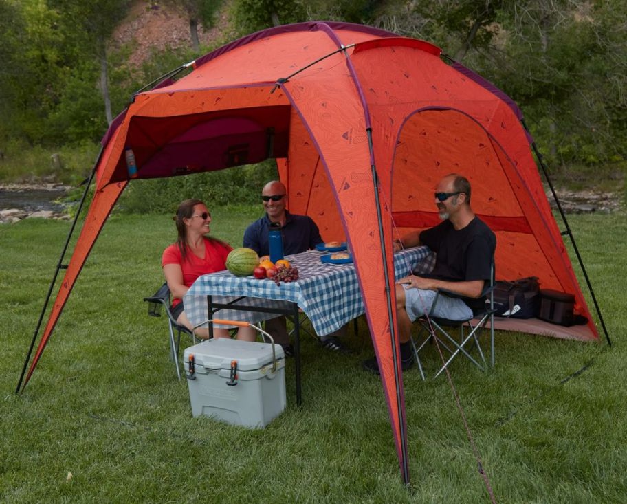 3 people sitting at a picnic table underneath a beach tent