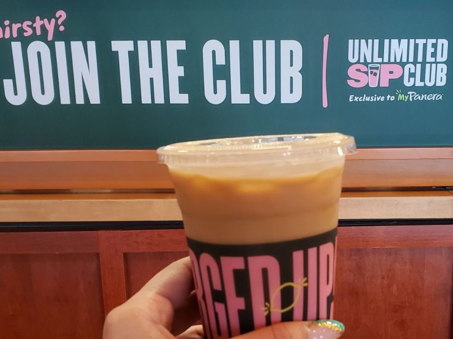 hand holding up a coffee in front of a panera sip club sign