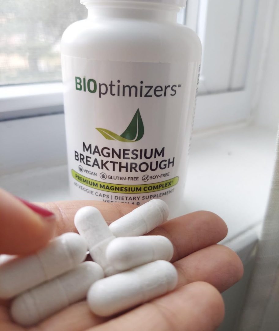 hand holding white capsules with magnesium bottle in background