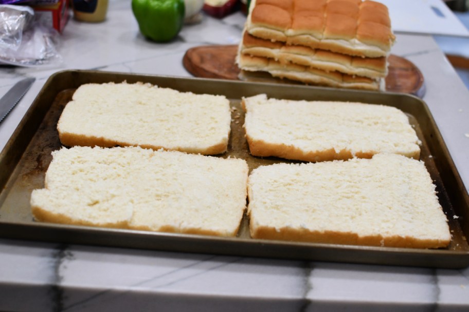 cutting the tops off of hawaiian rolls on a sheet pan