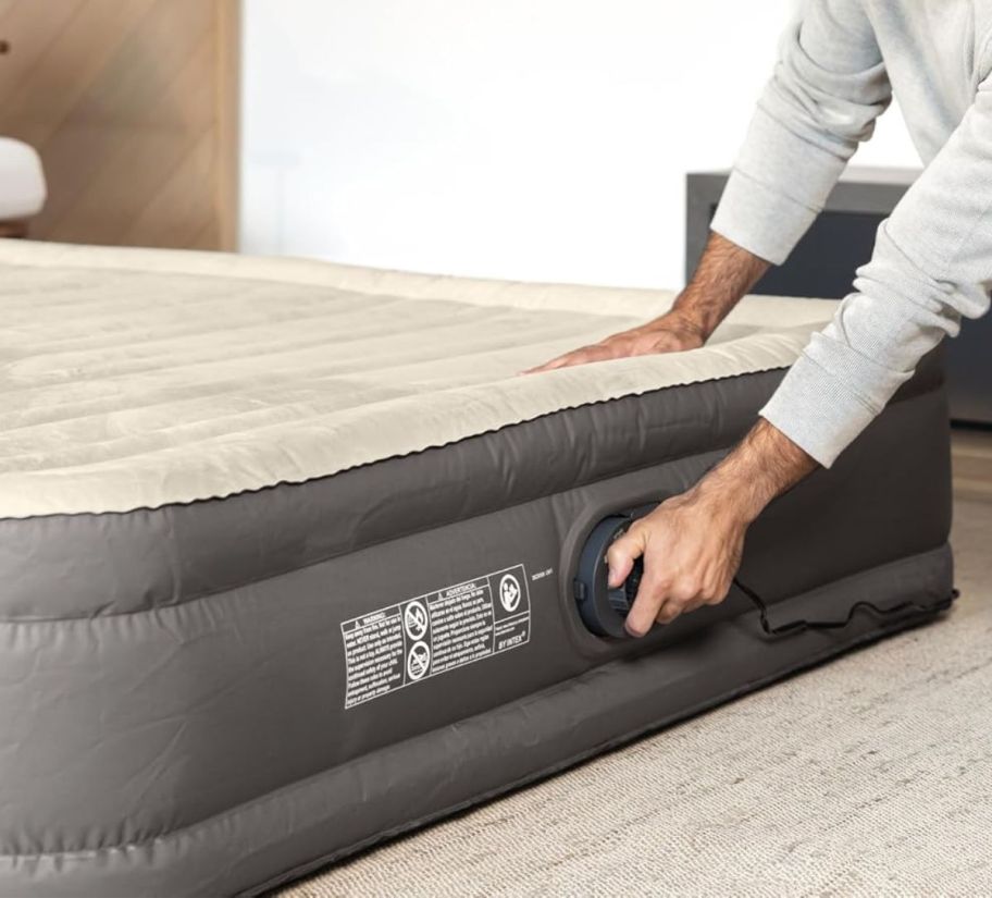 a man deflating an inflated queen size air mattress on a living room floor