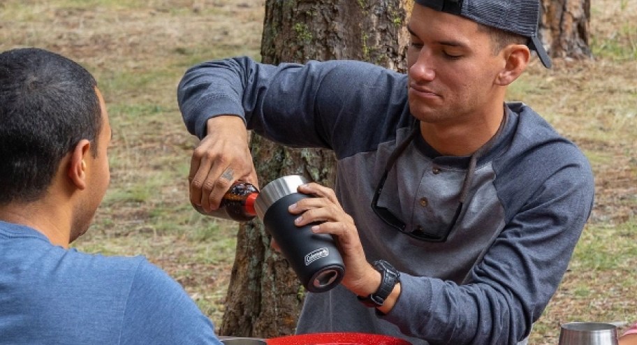 man pouring drink into coleman tumbler