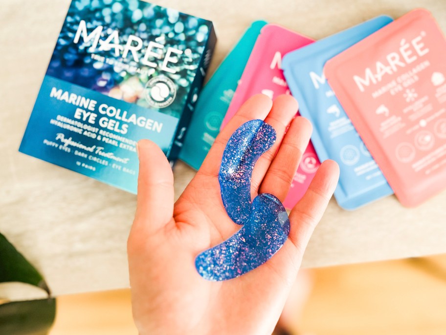 hand holding blue eye gels with packages on table underneath