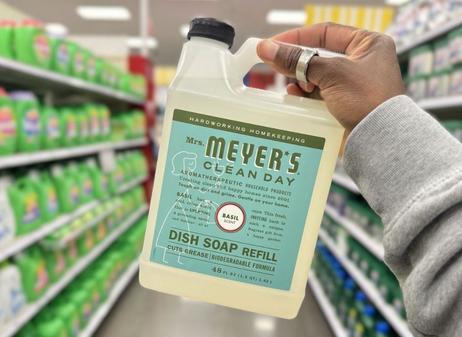 a womans hand holding a bottle of mrs meyers dish soap refill