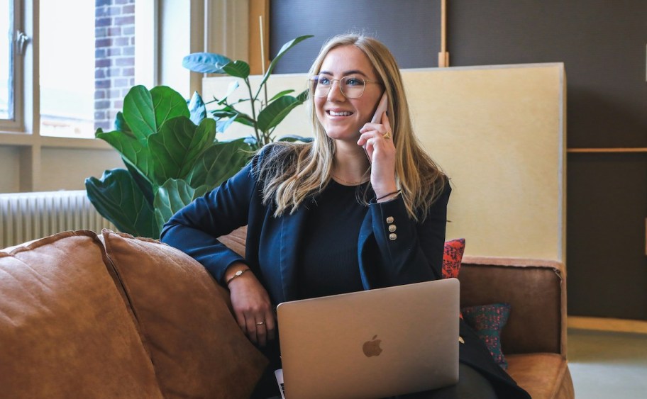 woman talking on phone sitting on leather couch with laptop on her lap