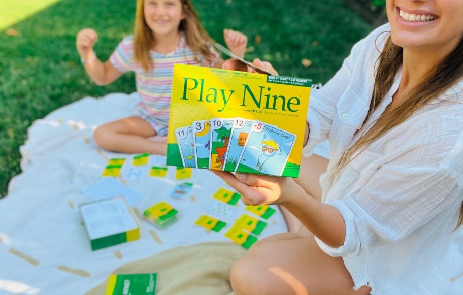 woman holding a Play Nine Card Game box, little girl in the background excited to play