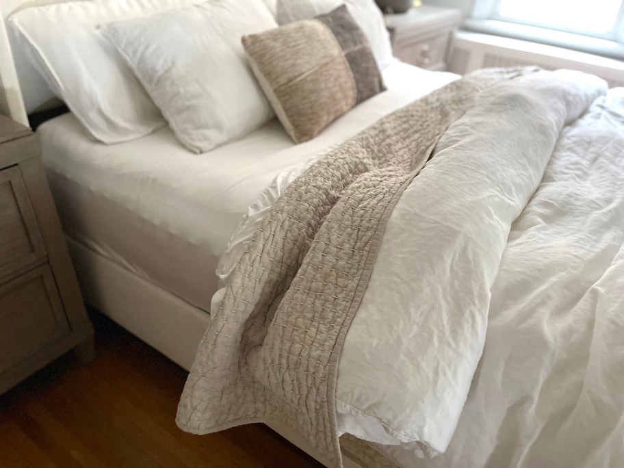 close up of made bed with white duvet and beige stitched quilt