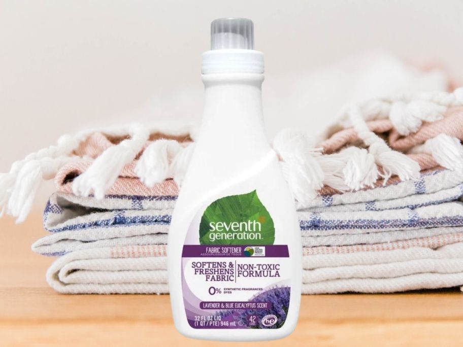 Seventh Generation Liquid Fabric Softener 32oz in Fresh Lavender bottle on table in front of a stack of towels