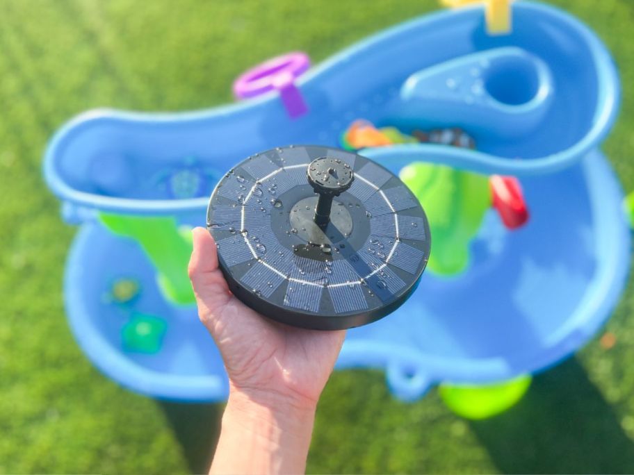 a womans hand holding a solar fountain with a water table in the background