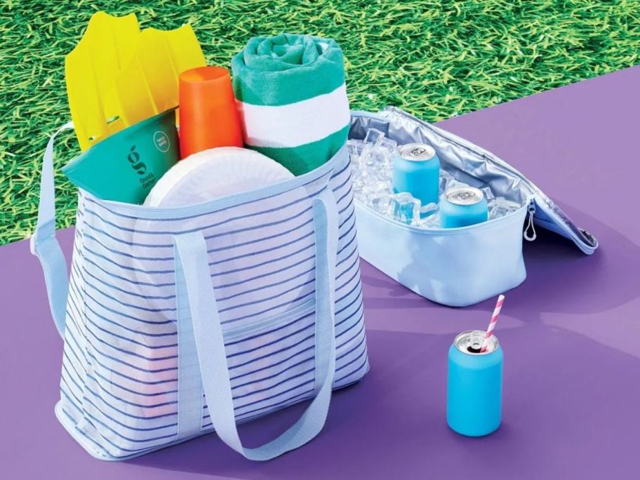 striped mesh tote bag with beach towels and lotion in it next to a cooler bag with soda and ice