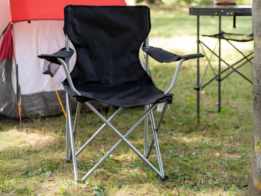 black camping chair sitting outside with a tent behind it