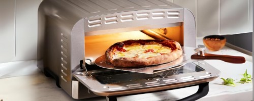 a stainless steel indoor pizza oven with a fresh baked pizza being pulled out of it