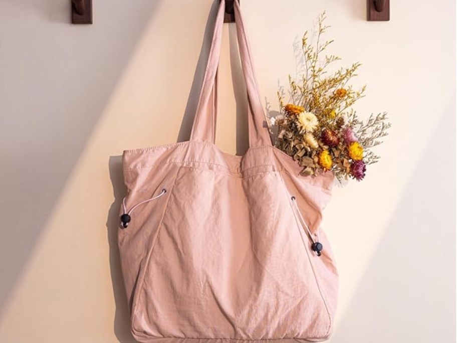 light pink fabric tote bag hanging from a wall hook with flowers in it