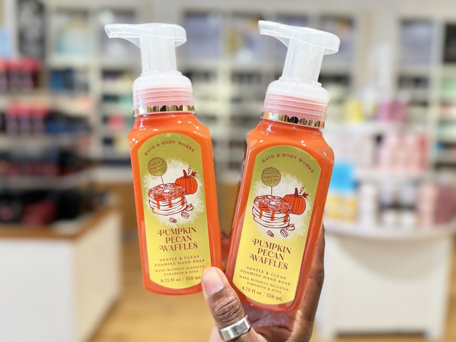 hand holding up two orange bath & body works hand soaps in pumpkin pecan waffles scent