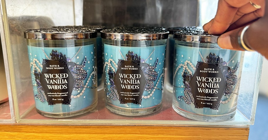 hand touching blue single wick candles in wicked vanilla woods scent