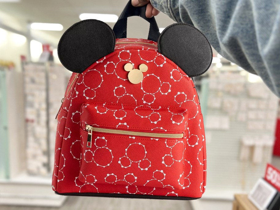 holding up a red backpack with mickey mouse print and mouse ears