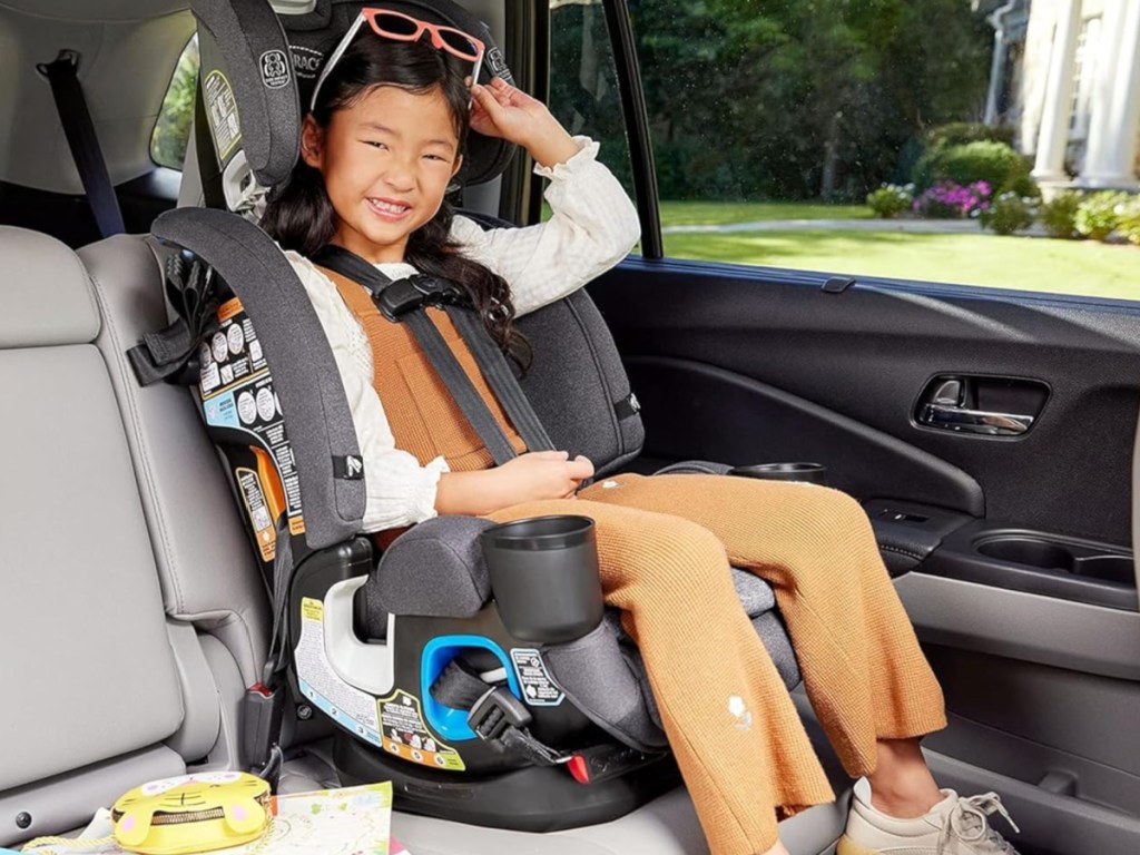 Small girl sitting in booster seat in car and smiling with sunglasses on top of her head