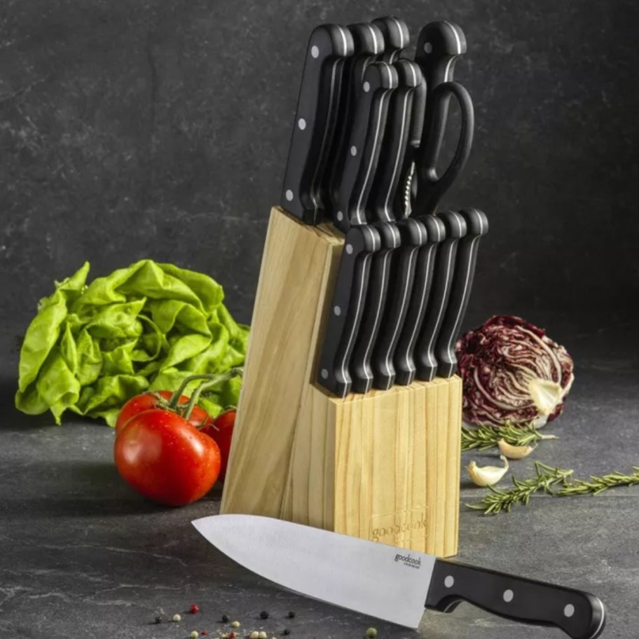 knife set with black handles in a wood block on a kitchen counter with a chef knife in front of it, food items around it