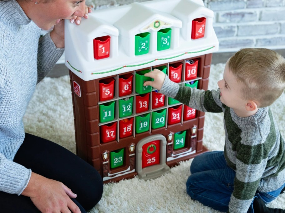 mom and little boy sitting by a large kid's advent calendar shaped like a house