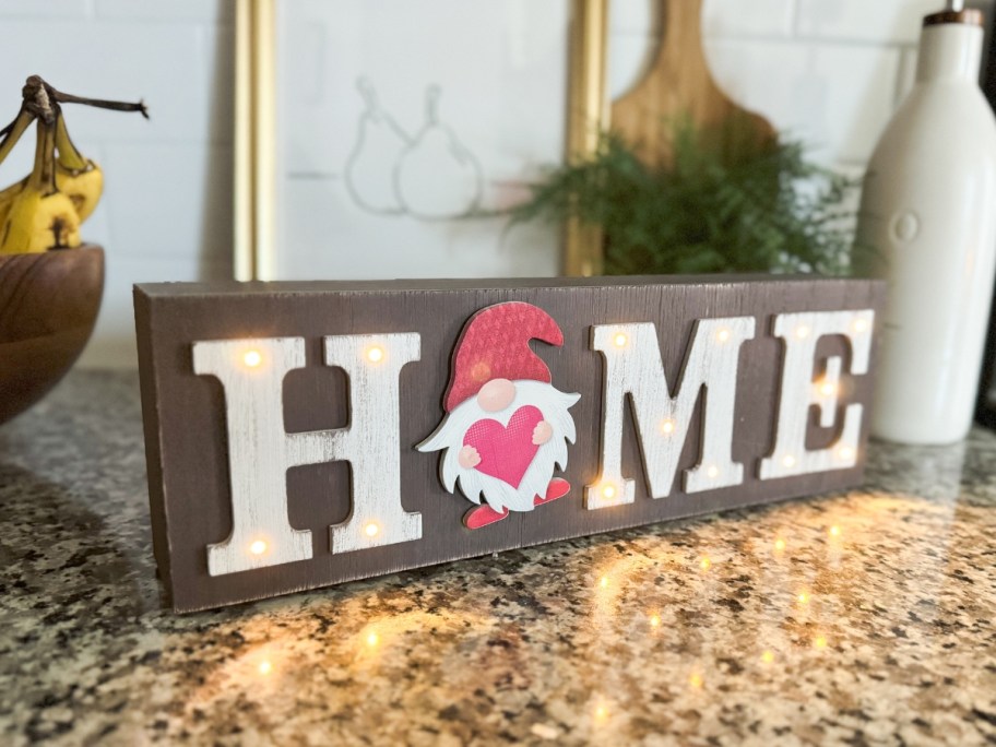 small wooden sign that says "Home" with a gnome on it sitting on a counter