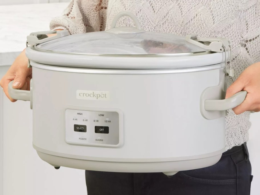 person carrying a large cream color Crockpot with the lid on it 