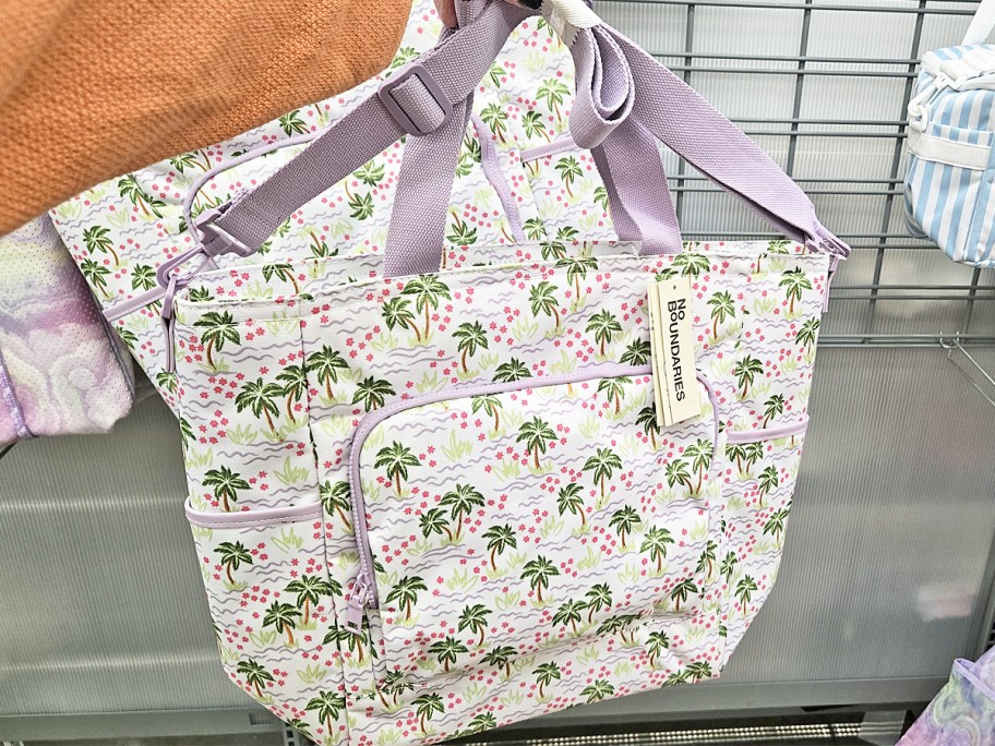 hand holding up white and purple floral print tote bag in store