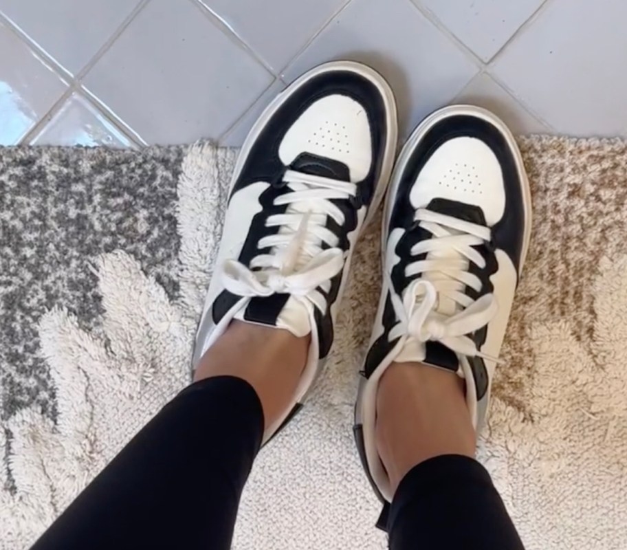 close up of black and white sneakers on feet standing on bathroom rug and tile floor